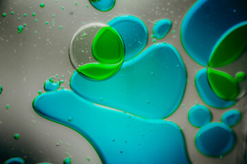 Vibrant green droplet encased in a blue fluid form, set against a neutral background with tiny...