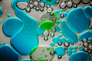 Vibrant green droplet encased in a blue fluid form, set against a neutral background with tiny...