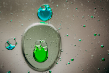 Vibrant green droplet encased in a blue fluid form, set against a neutral background with tiny...