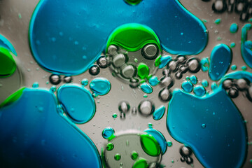 Vibrant green droplet encased in a blue fluid form, set against a neutral background with tiny suspended bubbles for added texture and depth.
