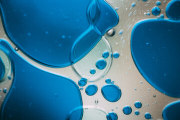 Vibrant green droplet encased in a blue fluid form, set against a neutral background with tiny suspended bubbles for added texture and depth.
