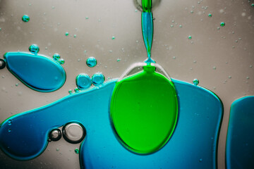 Vibrant green droplet encased in a blue fluid form, set against a neutral background with tiny suspended bubbles for added texture and depth.