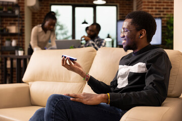 Young businessman seated on couch projects digital content in modern workspace. Behind him, black...
