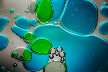 Vibrant green droplet encased in a blue fluid form, set against a neutral background with tiny...
