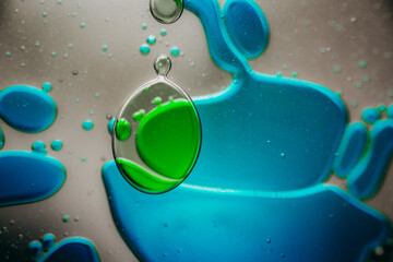 Vibrant green droplet encased in a blue fluid form, set against a neutral background with tiny...