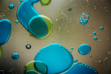 Vibrant green droplet encased in a blue fluid form, set against a neutral background with tiny...