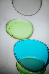 Vibrant green droplet encased in a blue fluid form, set against a neutral background with tiny...
