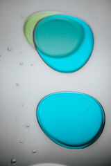Vibrant green droplet encased in a blue fluid form, set against a neutral background with tiny suspended bubbles for added texture and depth.