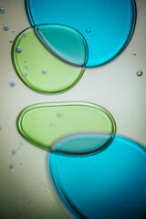 Vibrant green droplet encased in a blue fluid form, set against a neutral background with tiny suspended bubbles for added texture and depth.
