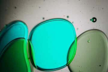 Vibrant green droplet encased in a blue fluid form, set against a neutral background with tiny suspended bubbles for added texture and depth.
