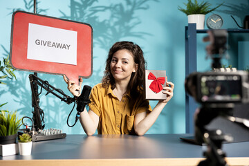 Social media influencer announcing giveaway for audience with cardboard sign, holding gift box,...