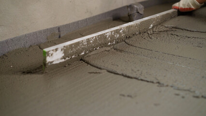 Construction worker leveling concrete floor with trowel