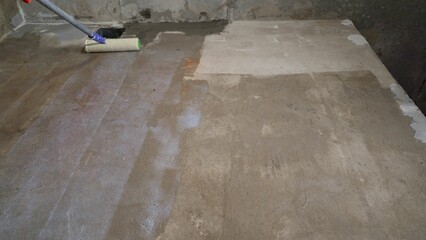 Construction worker applying waterproofing coating on concrete floor using roller