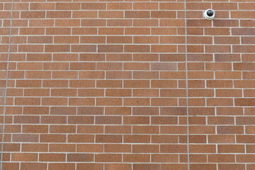 Red brick wall with security camera in upper right corner.