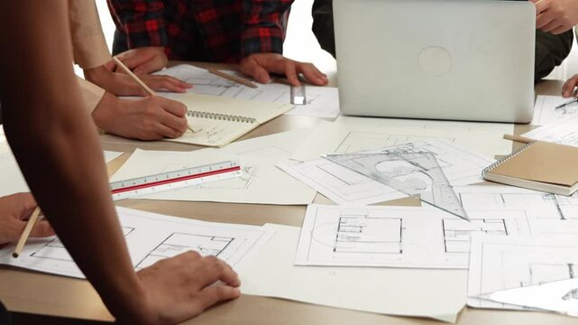 Architect and safety engineer discussion about building blueprint displaying on laptop on table with architectural document and wooden block scatter around at modern office. Closeup. Delineation.