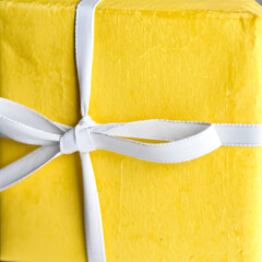 Close-up view of a bright yellow gift box tied with a white ribbon, beautifully presented.