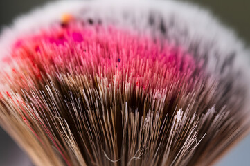 Close-up of a makeup brush bristles, stained with vibrant pink and other colors, showing detail and texture.