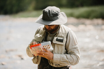 Angler examining fishing lures by riverside