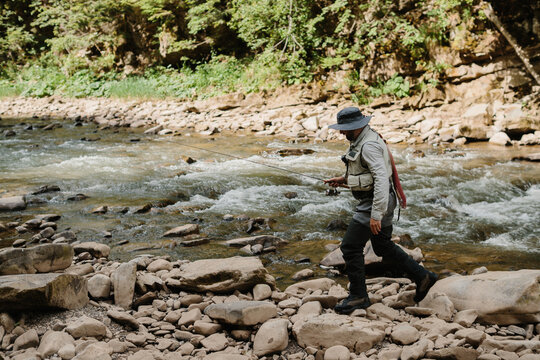 Fisherman walking on rocks while fishing in river - Powered by Adobe