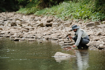 Fisherman catching trout in river with fishing rod and landing net