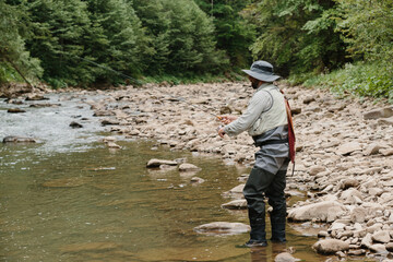 Fisherman catching trout in river, fly fishing in mountain stream