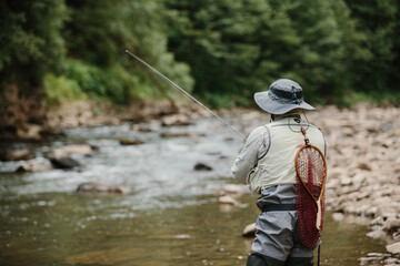 Fisherman catching trout in a mountain river with fishing rod