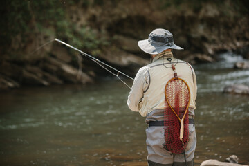 Fisherman with fishing rod and net catching trout in river