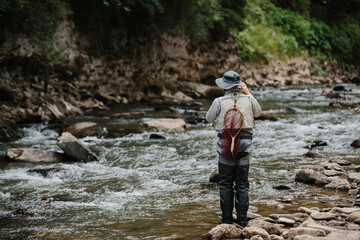 Fisherman with fishing rod and net catching trout in river
