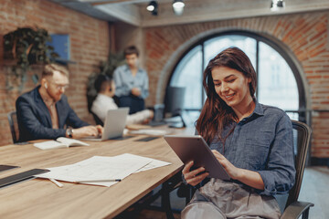 A professional team engages in a meeting while using digital devices in a contemporary office...