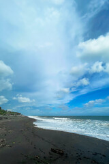 View of a dramatic cloudy sky over remote black sand shoreline. Peaceful tropical scene perfect for nature, travel, solitude, and coastal mood.