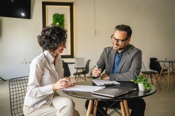 Mature woman sign insurance or contract to adult man in cafe