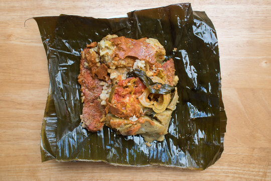 Traditional Nicaraguan nacatamal opened to reveal tasty filling of seasoned meat and vegetables inside corn dough wrapped in banana leaf.