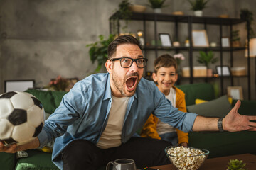 Father and son watch football match and cheer at home