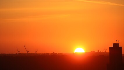 Naklejka premium A serene sunset cityscape with golden hues, featuring distant urban silhouettes and a soft gradient sky.