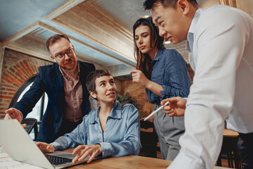 A diverse team is actively engaging in a collaborative brainstorming session over a laptop in a...