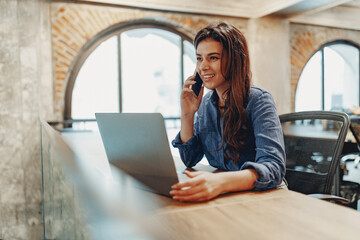 A dedicated woman is thoroughly engaged in her work while using both a laptop and a phone in a...