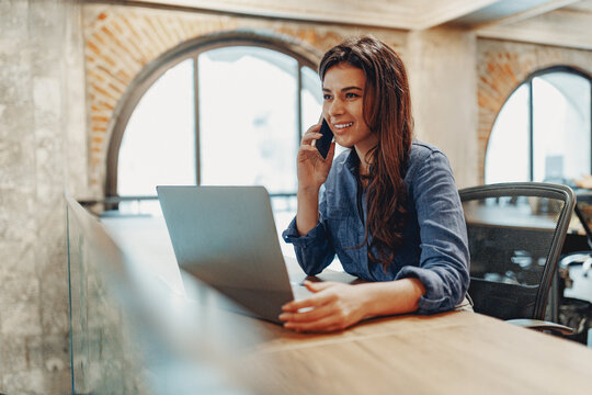 A dedicated woman is thoroughly engaged in her work while using both a laptop and a phone in a modern office setting - Powered by Adobe