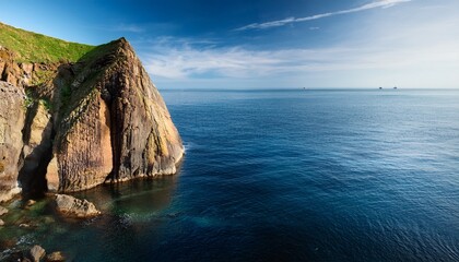 rocky cliff rises above calm blue ocean