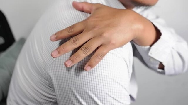 Holding a sore shoulder. A man has a shoulder injury and joint pain. Close-up of the man sitting on a sofa massaging his shoulder with his hand. Shoulder pain due to frozen shoulder.