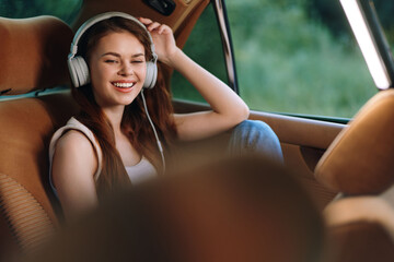 Young woman joyfully listening to music in a car, wearing headphones and a casual outfit,...