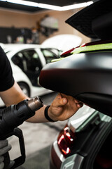 Car Vinyl Wrapping with Heat Gun. Applying black vinyl wrap to car with heat gun ensures precise...