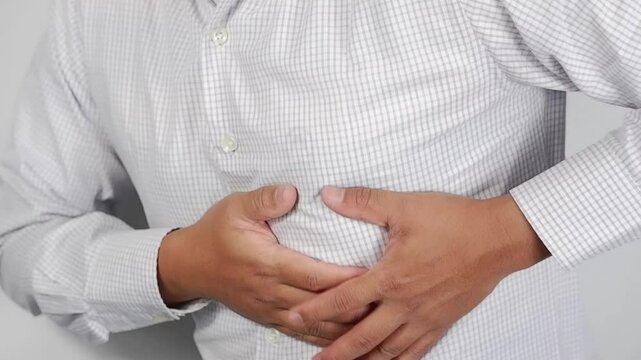 Sick Asian man experiencing abdominal pain, pain and discomfort, severe abdominal pain, left kidney infection or appendicitis, pain in the left side of the abdomen, squeezing the abdomen with an expre