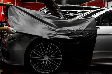 Car wrapping process using black matte vinyl stretched into place. Careful application and tensioning of black vinyl avoids surface damage or bubbling. Matte black vinyl is applied across car hood.