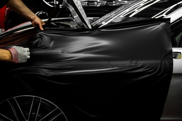 Car wrapping process using black matte vinyl stretched into place. Careful application and...
