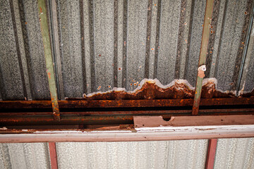 A weathered metal structure exhibiting substantial rust and deterioration, featuring a corrugated...