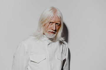 Senior man with long white hair, looking contemplative against a plain grey background Stylish,...
