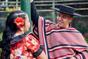 Portrait of a smiling young couple, dressed as Chilean huasos, looking at each other and posing...