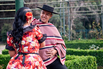 Portrait of a smiling young couple, dressed as Chilean huasos, looking at each other and posing...