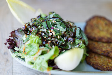 Frischer Salat, garniert mit Kernen und Dressing, serviert mit Reibekuchen / Kartoffelpuffe