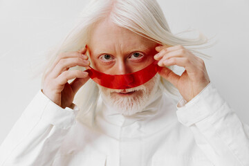 Elderly man with long white hair and beard holding a red ribbon, wearing a white outfit The...